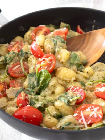 black skillet full of gnocchi and tomatoes in pesto cream sauce