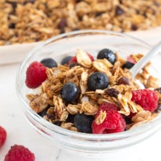 homemade granola in a clear bowl with raspberries and blueberries