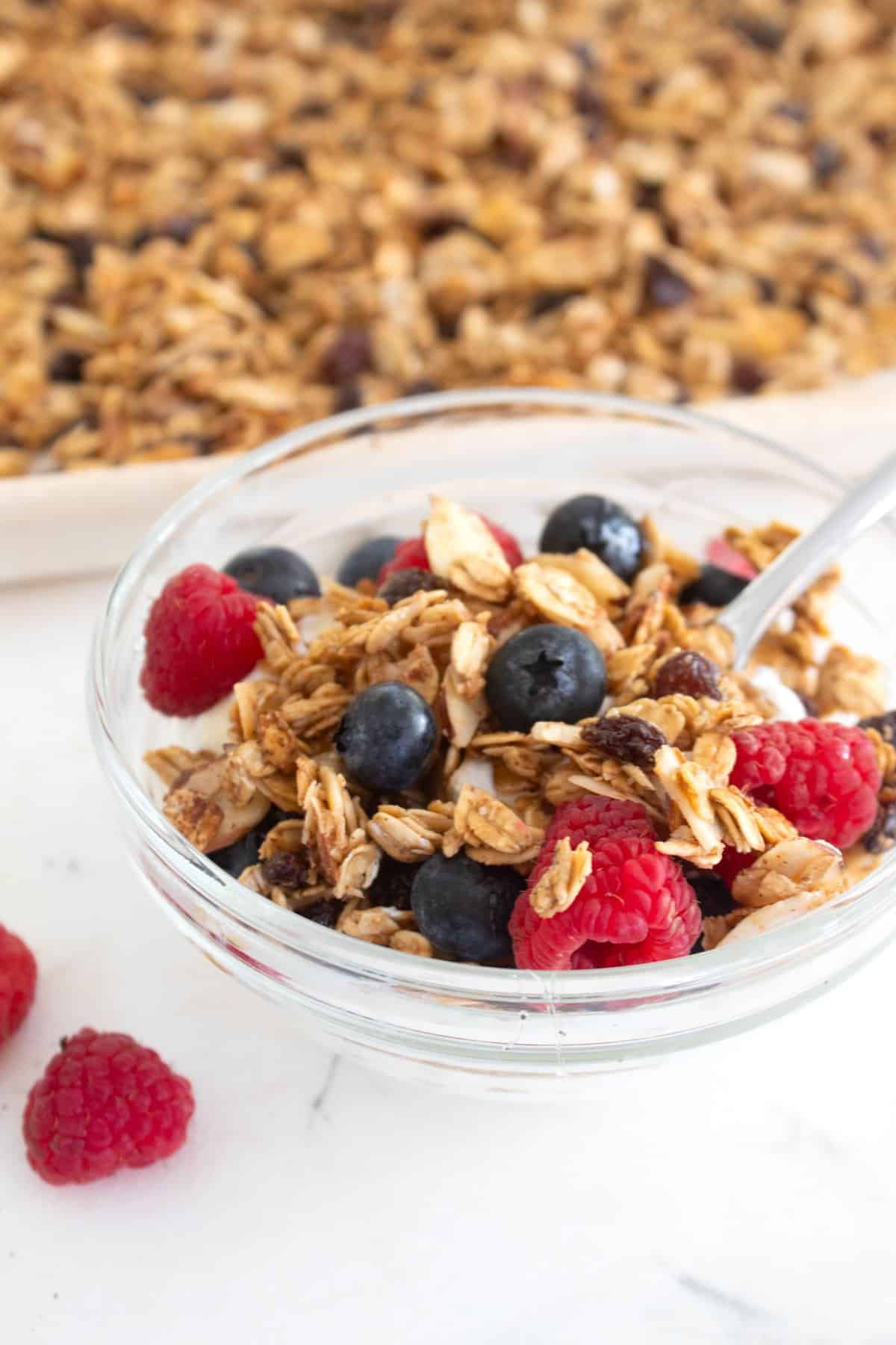 homemade granola in a clear bowl with raspberries and blueberries