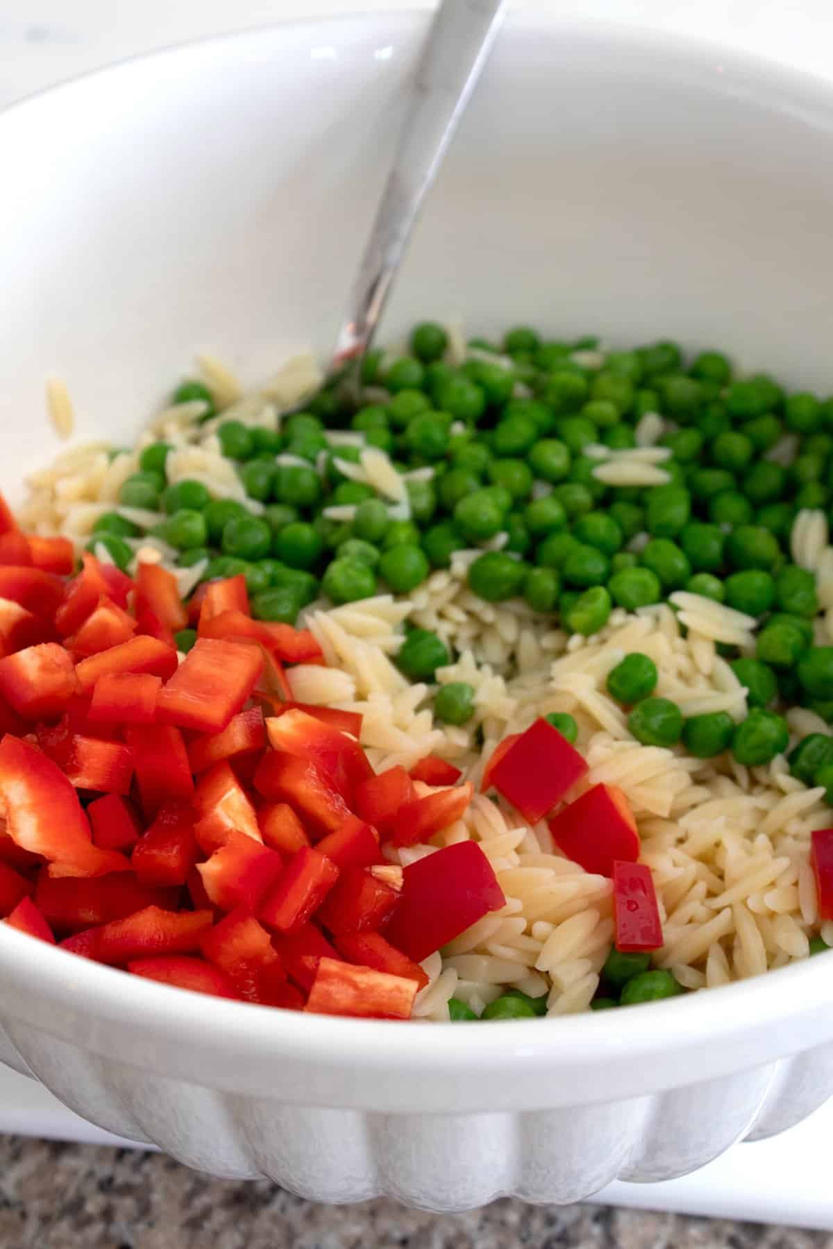 adding orzo, red bell pepper and peas to a bowl