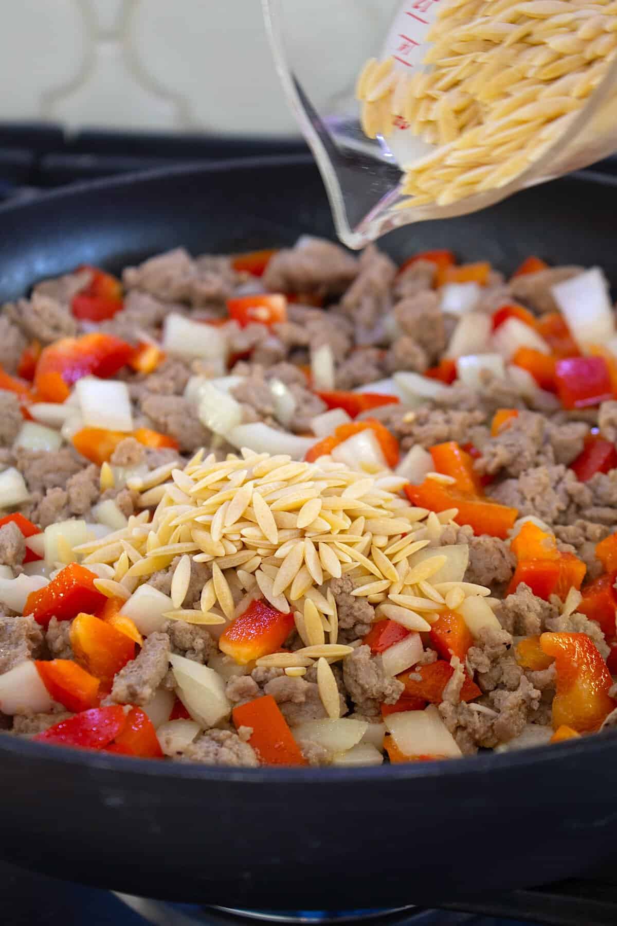 red bell pepper, onion and ground turkey in a skillet pouring dry orzo in
