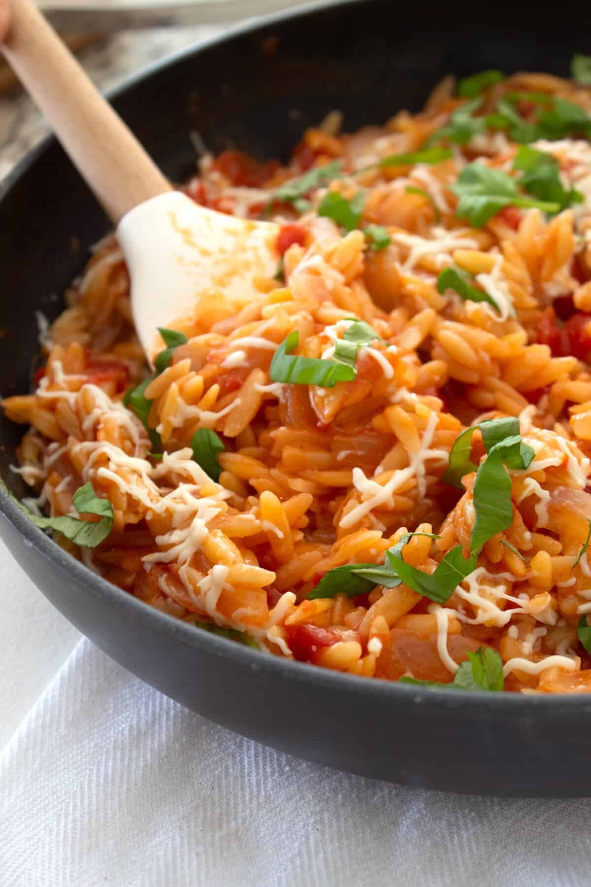 skillet pan full of tomato orzo garnished with mozzarella and basil