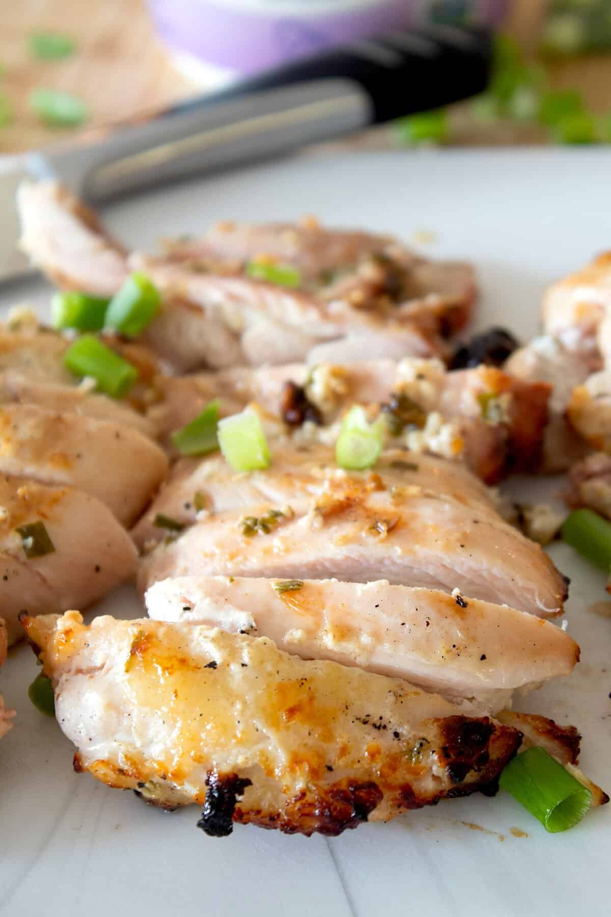 sliced yogurt marinated chicken on a cutting board with yogurt in background