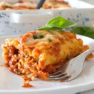 Lasagna roll up on a white plate with basil garnish