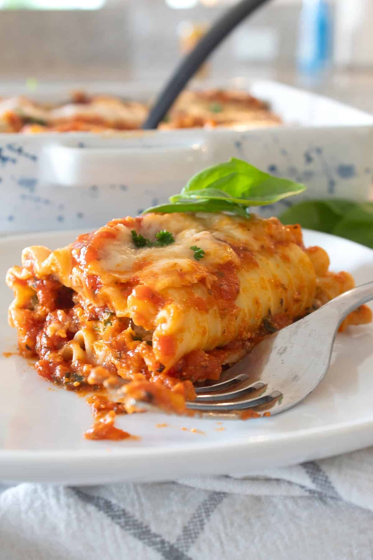 Lasagna roll up on a white plate with basil garnish