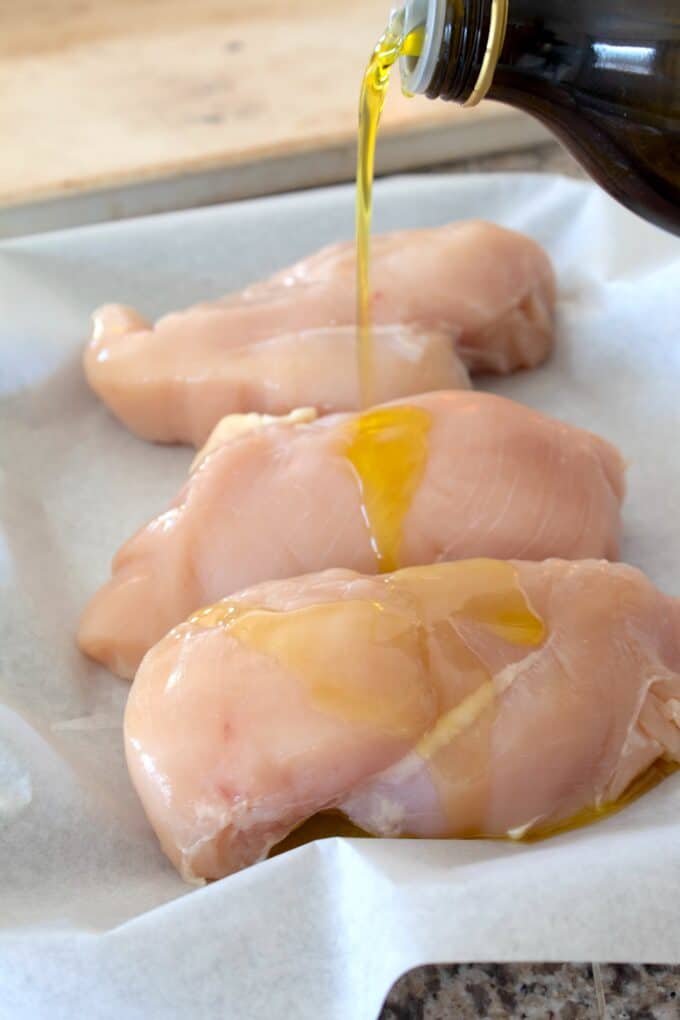 drizzling olive oil on chicken breasts on sheet pan