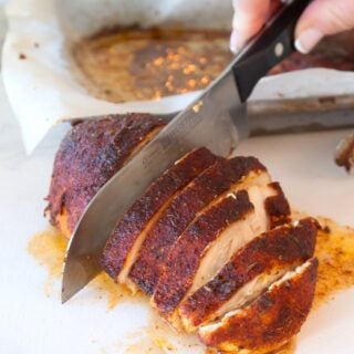 slicing baked blackened chicken on a white cutting board