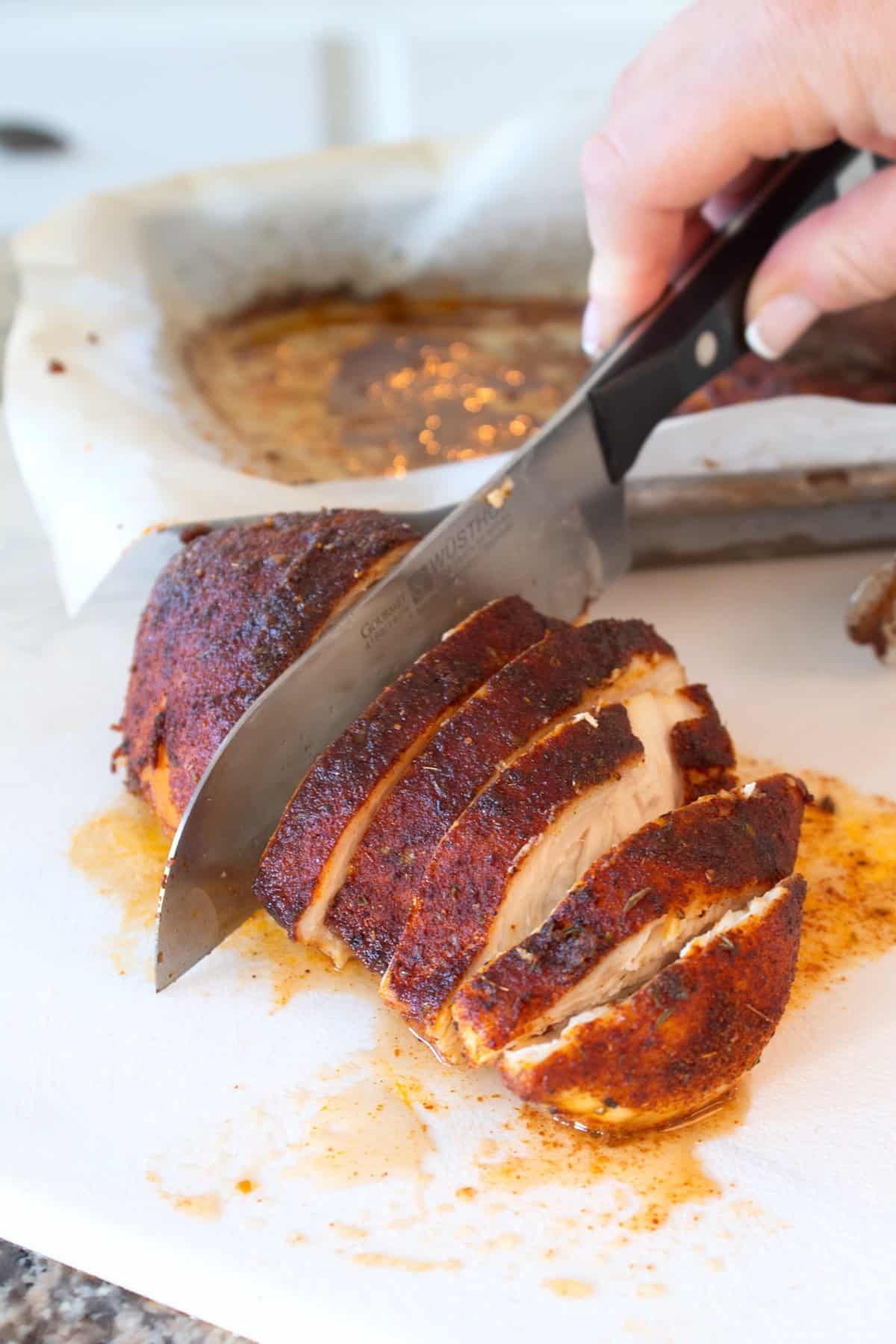 slicing baked blackened chicken on a white cutting board