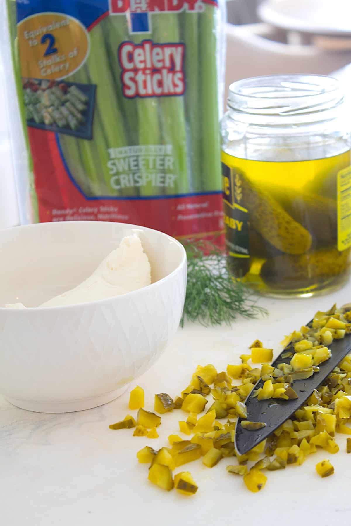 chopping pickles for pickle dip on a white cutting board