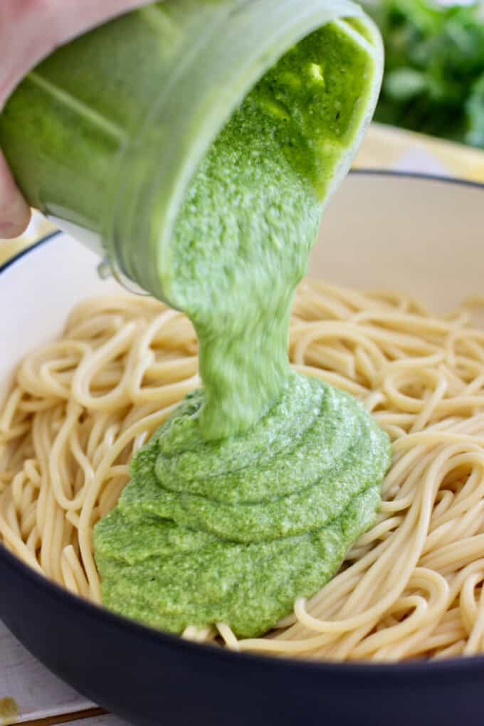 pouring green sauce over cooked spaghetti