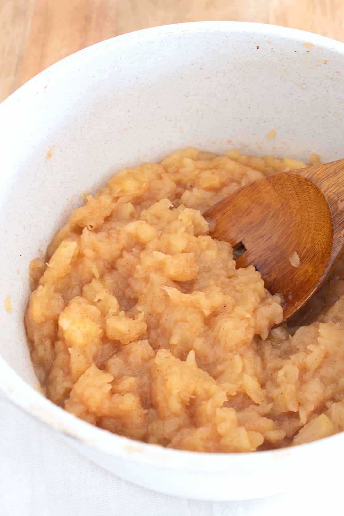 mashing applesauce in a pot with a wooden spoon