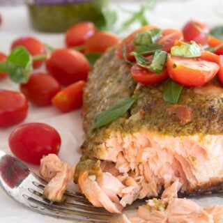 pesto coated salmon on a sheet pan with tomatoes and basil