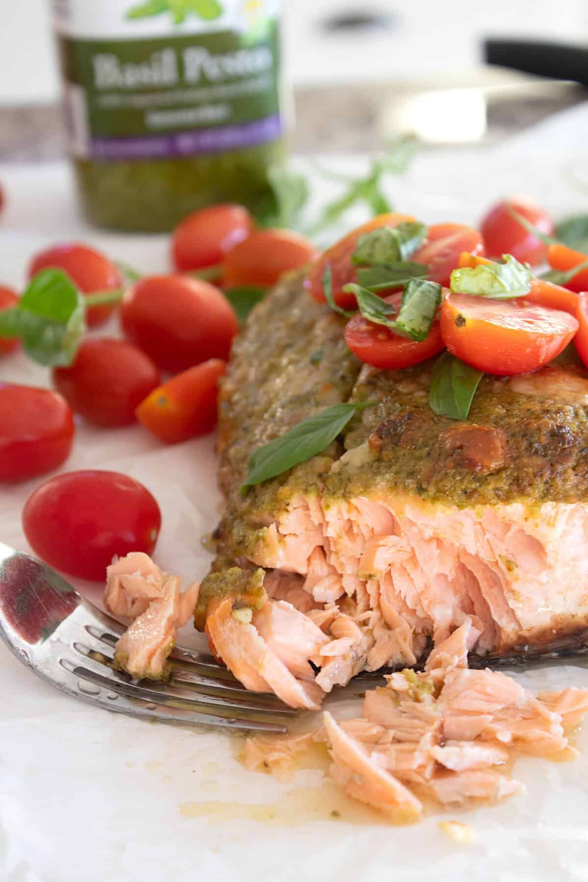 pesto coated salmon on a sheet pan with tomatoes and basil