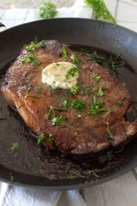 overhead view of steak in a pan with compound butter and parsley