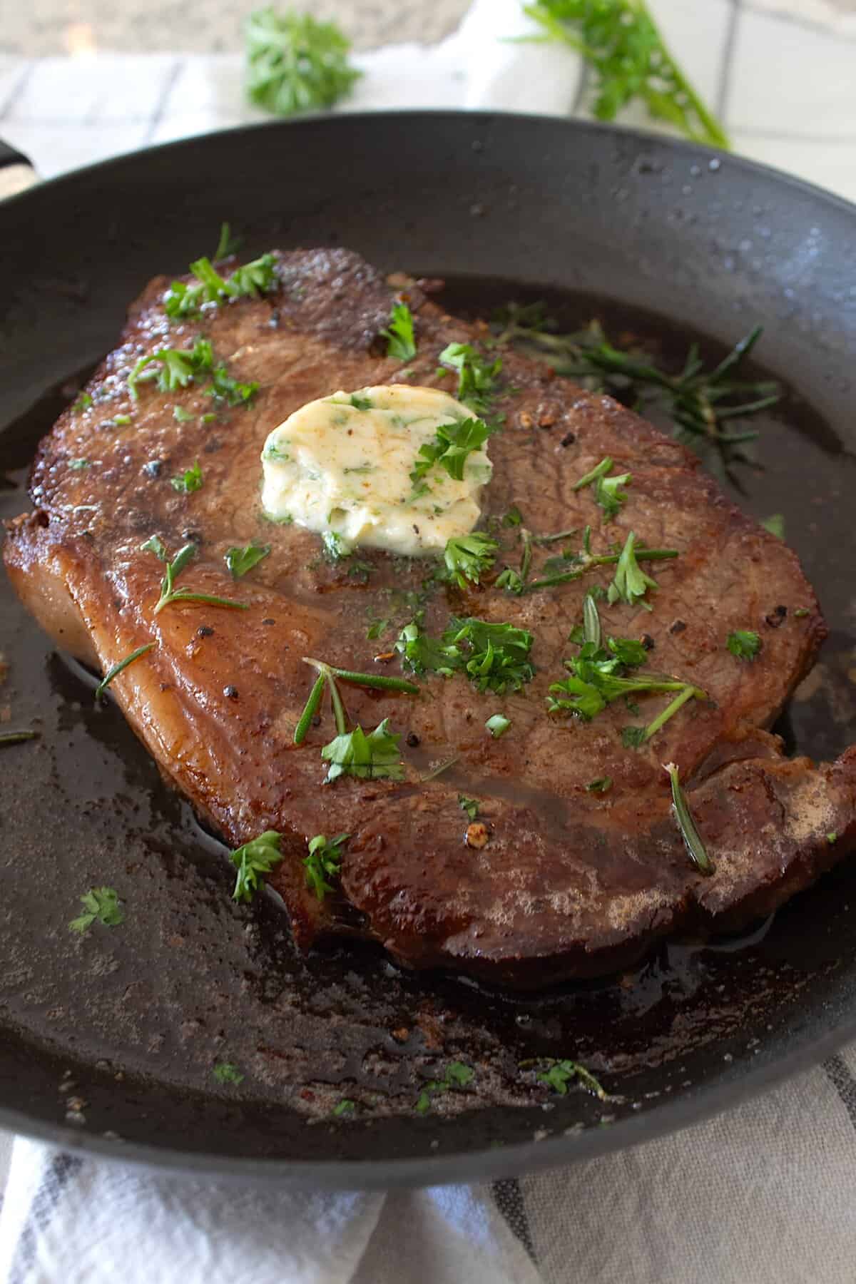 overhead view of steak in a pan with compound butter and parsley