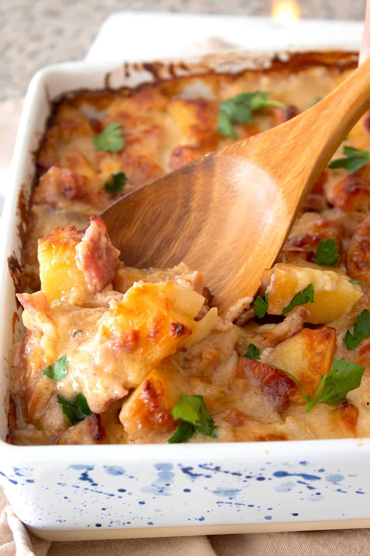 ham and potato casserole in a dish with a wooden spoon scooping casserole