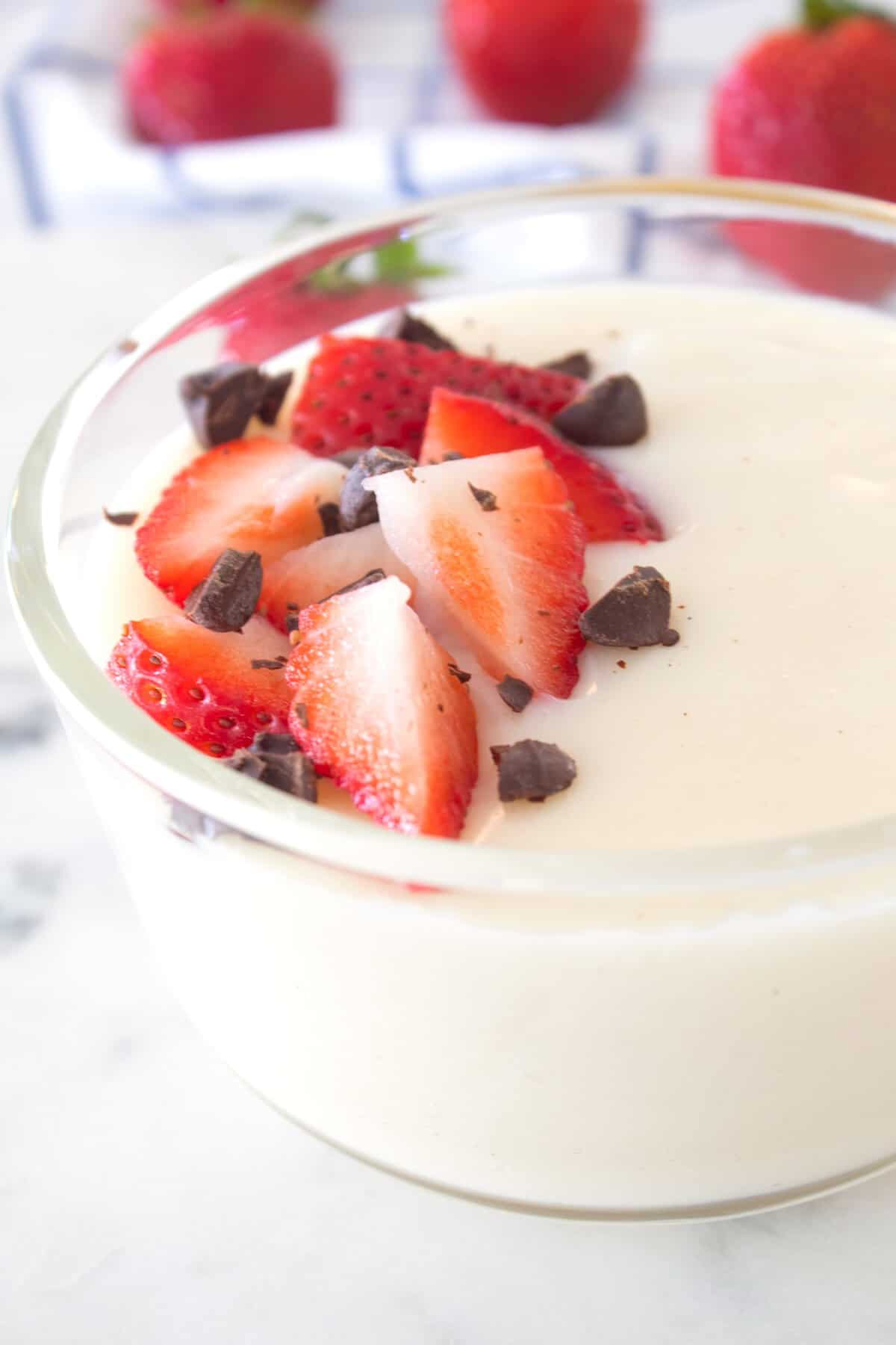 bowl full of vanilla pudding with chocolate and strawberry garnish