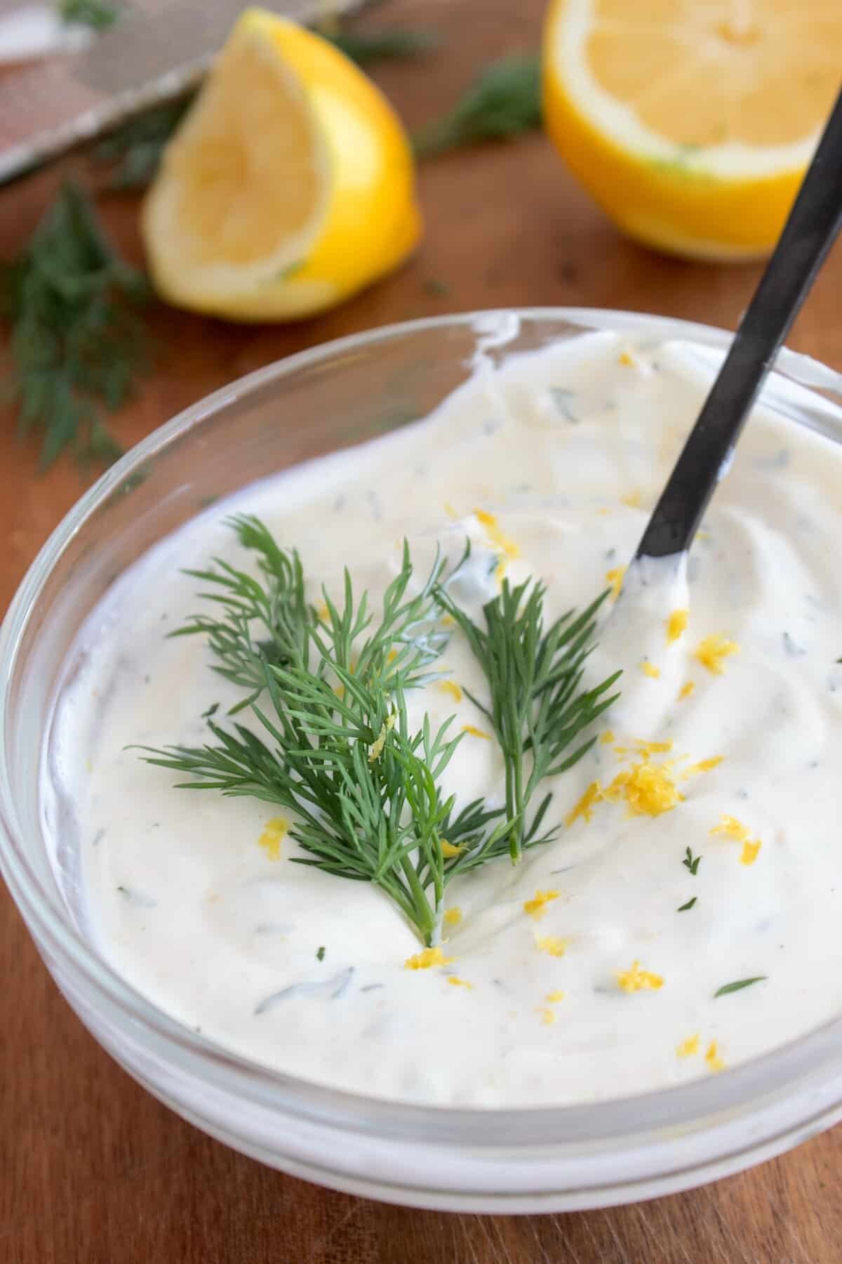 Dill sauce in a clear bowl with lemons in background