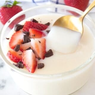 vanilla pudding in a clear dish with strawberries and chocolate garnish and a gold spoon spooning some