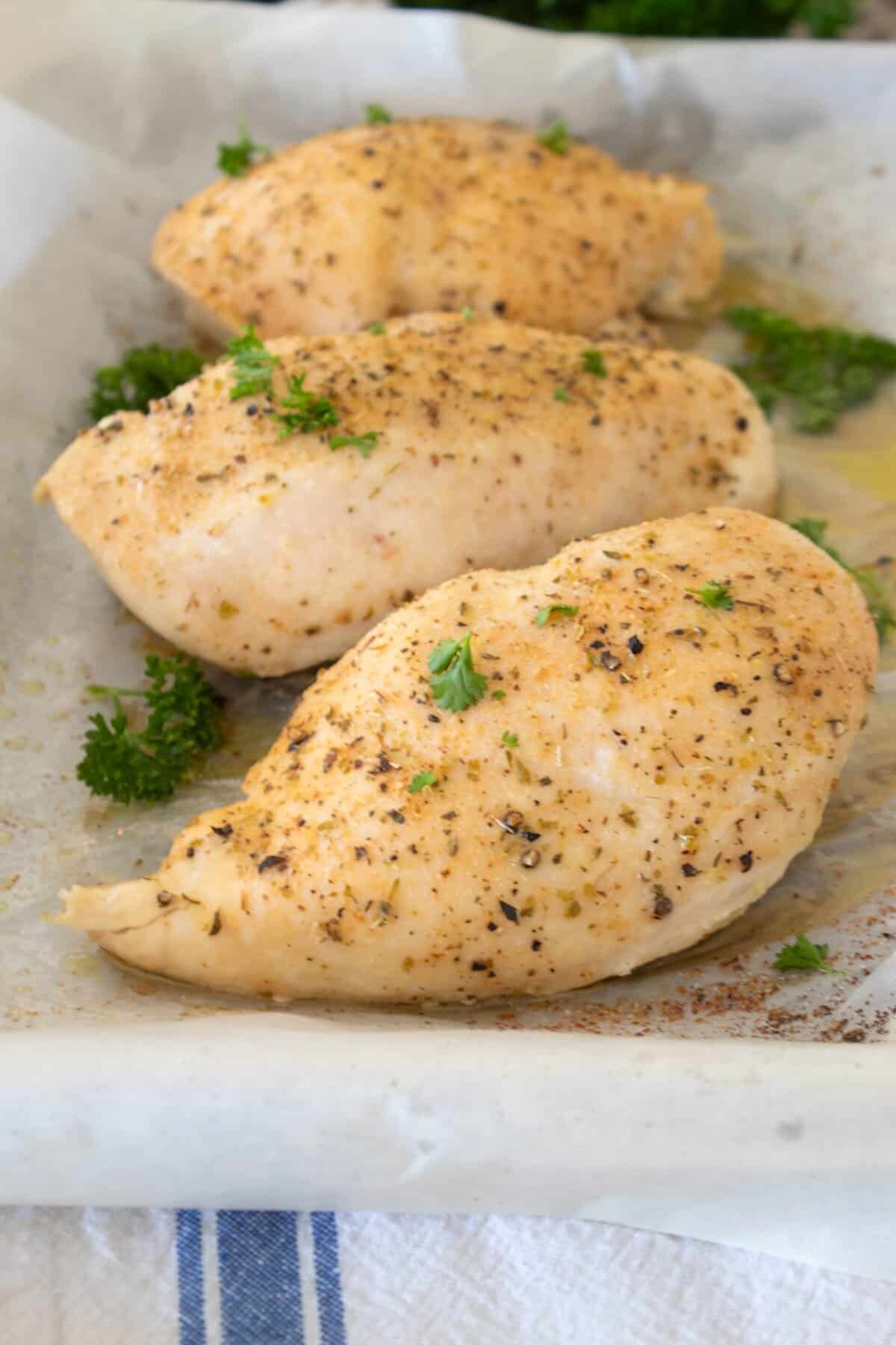 sheet pan with 3 chicken breasts on it garnished with parsley