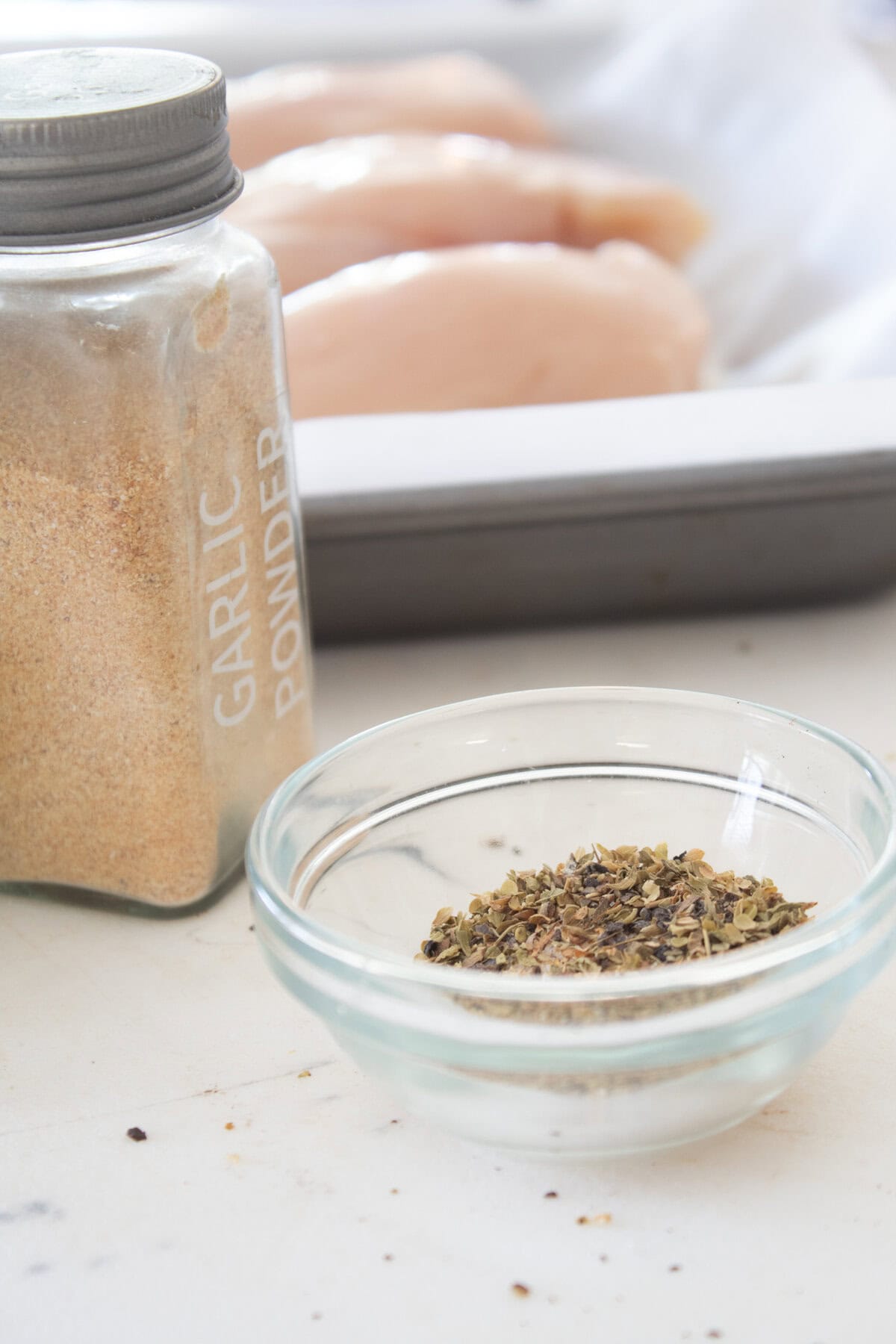 seasoning for baked chicken breasts in a small glass container with raw chicken breasts in the background 