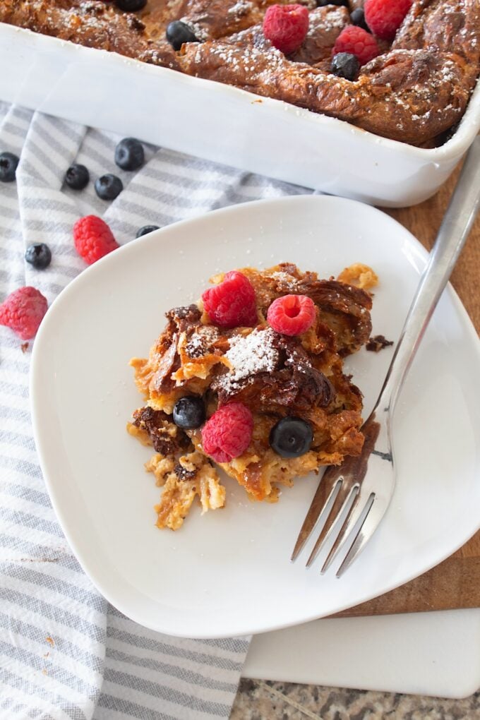 overhead view of French toast croissant casserole on a white plate with berries scattered in the background