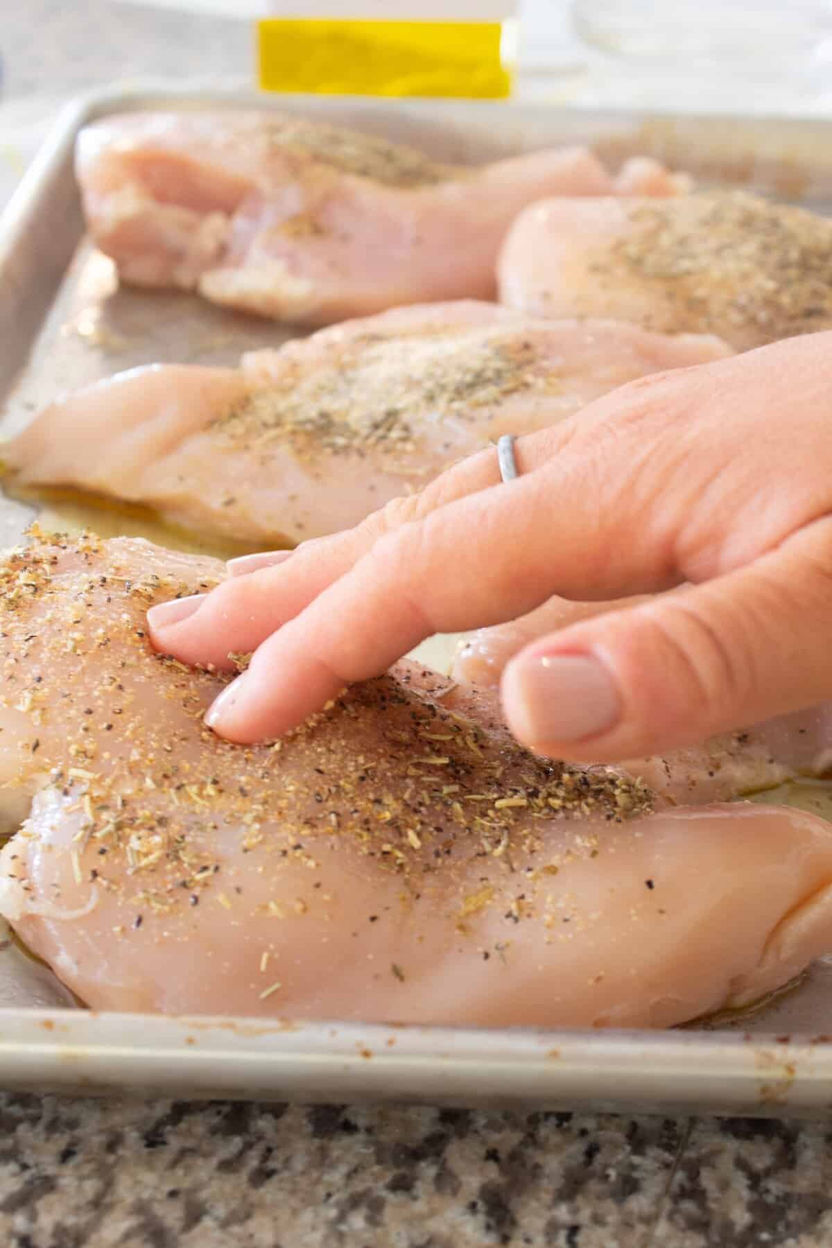 seasoning chicken breasts with hand