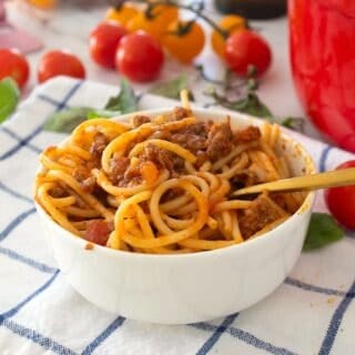 spaghetti in a bowl with tomatoes in the background