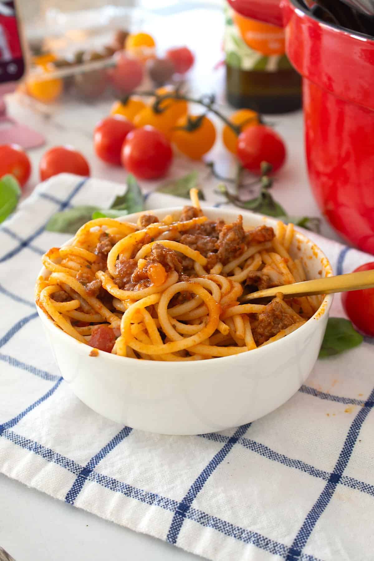 spaghetti in a bowl with tomatoes in the background
