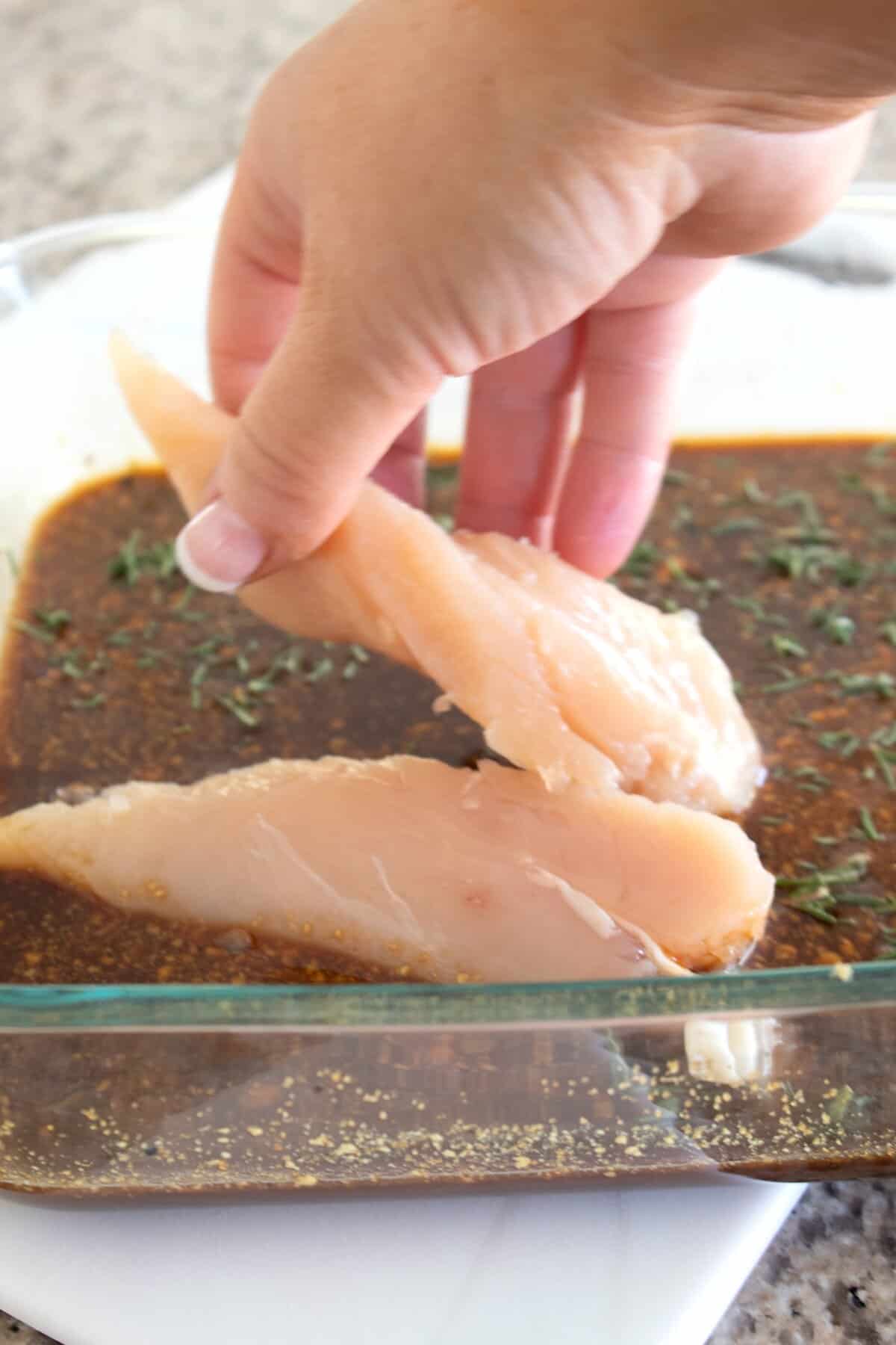 adding chicken tenders to marinade pyrex dish