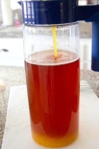 pouring mango puree in a gallon pitcher of iced tea