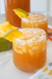 mango iced tea in a clear short glass with mango slice garnish