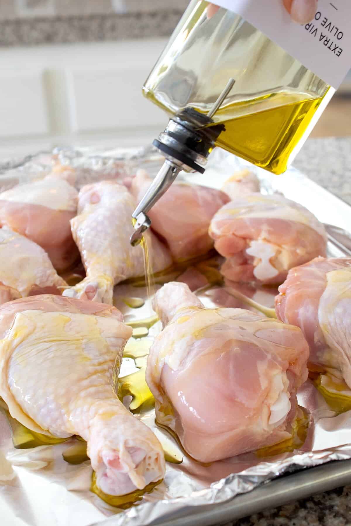 adding olive oil to chicken drumsticks on sheet pan