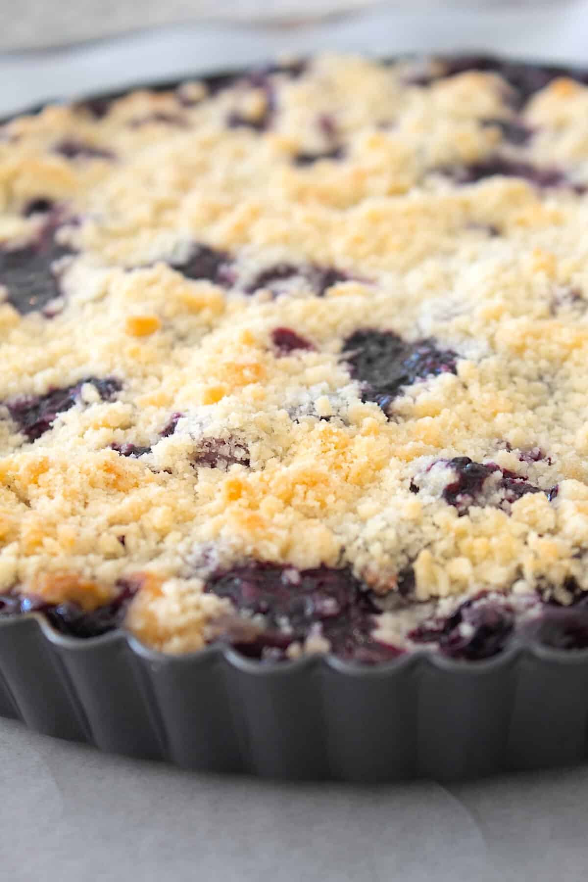removing blueberry crumb bars from oven in a pie tart pan