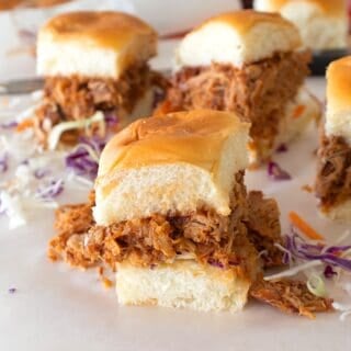 BBQ chicken sliders on parchment with cabbage slaw in background