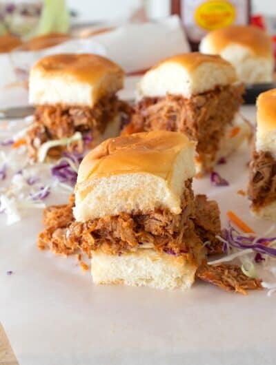 BBQ chicken sliders on parchment with cabbage slaw in background