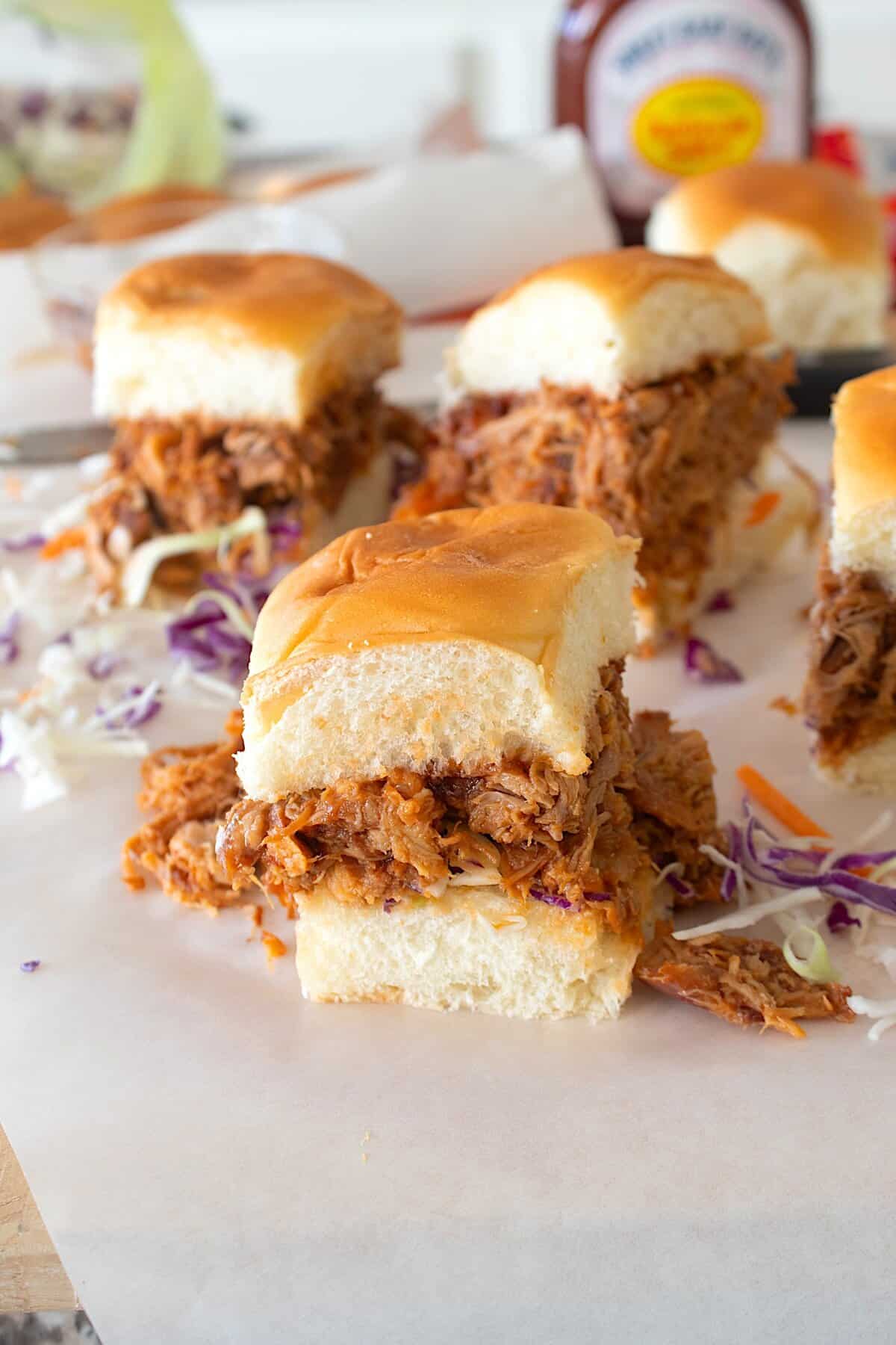 BBQ chicken sliders on parchment with cabbage slaw in background