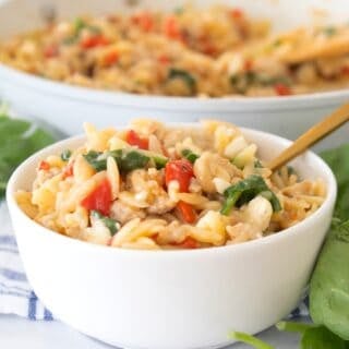 tuscan orzo in a white bowl with a skillet in the background