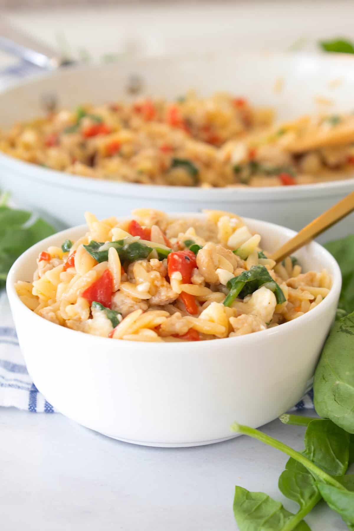 tuscan orzo in a white bowl with a skillet in the background